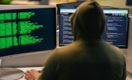 Hacker in hoodie working on multiple computer screens